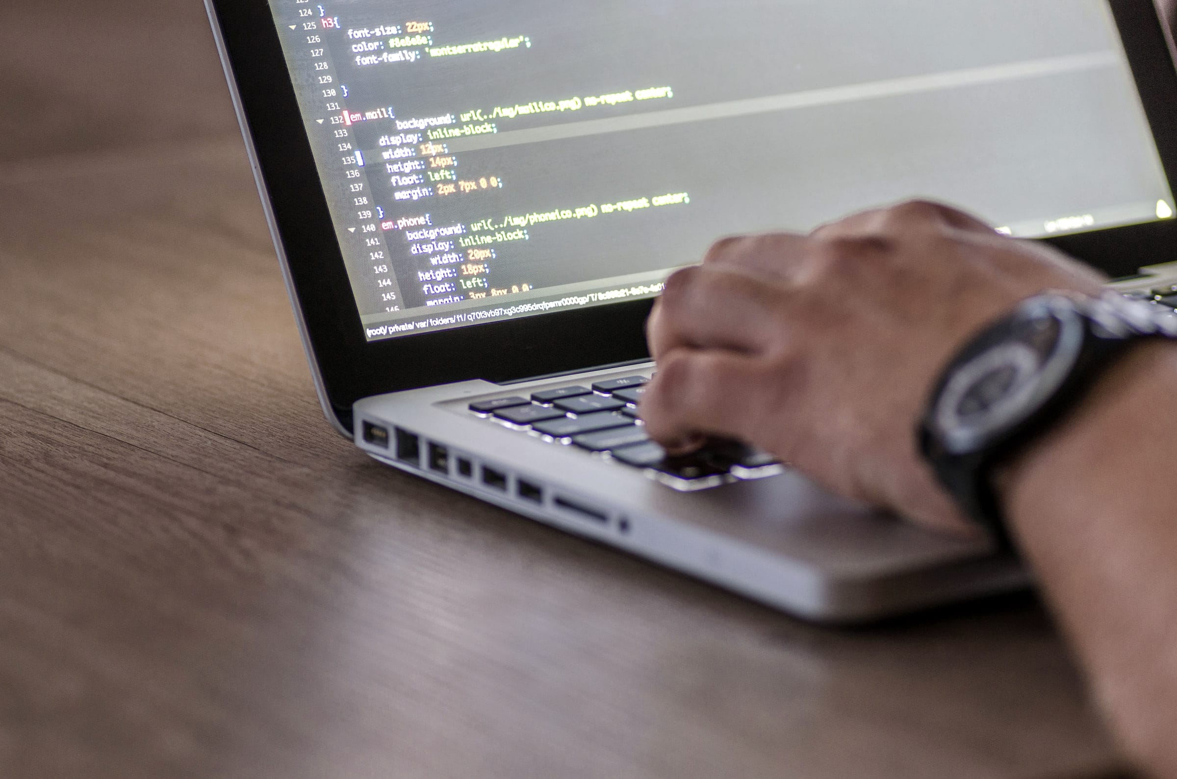 Hands at a laptop keyboard with code on the screen.