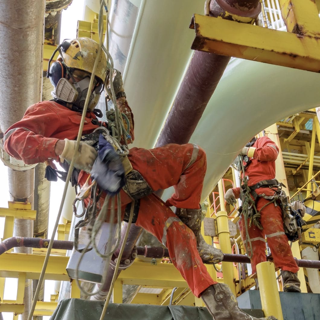 A rope-access technician in a respirator and harness, clipped to an offshore structure.